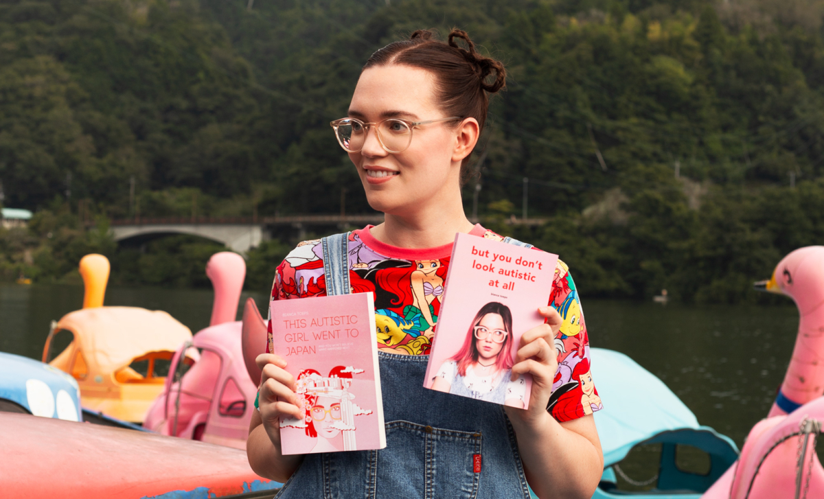 Bianca Toeps holding But You Don't Look Autistic At All and This Autistic Girl Went to Japan at Lake Sagamiko, with swan boats in background